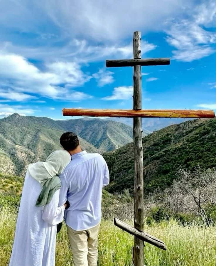 A couple on a hillside beside a wooden cross